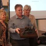 Christine Cunningham, left, and Mary Bondurant, right, both members of the Kenai Bronze Bear Sculpture Working Group, stand for a photo with Kenai Mayor Brian Gabriel and a small model of the proposed sculpture during a luncheon hosted by the Kenai Chamber of Commerce in Kenai, Alaska, on Wednesday, March 19, 2025. (Jake Dye/Peninsula Clarion)