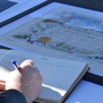 An attendee of the decommissioning ceremony signs the vessels guest book on Friday, March 21, 2025, on Freight Dock Road on the Homer Spit in Homer, Alaska. (Chloe Pleznac/Homer News)