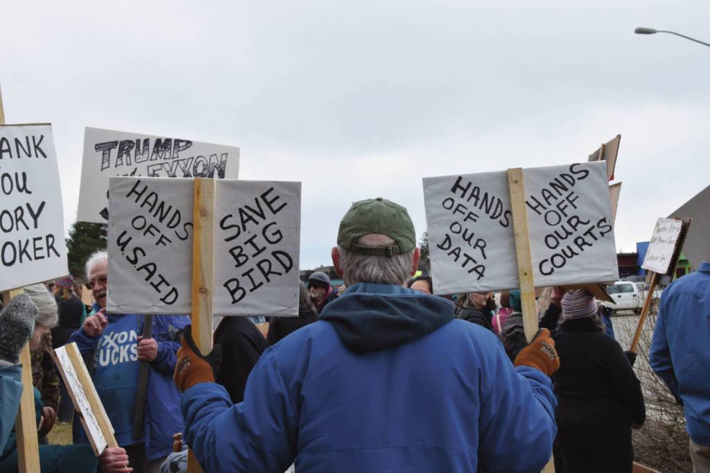 A protester in Homer holds up signs during the nationwide Hands Off! protest on Saturday, April 5 at WKFL Park in Homer, Alaska. (Chloe Pleznac/Homer News)