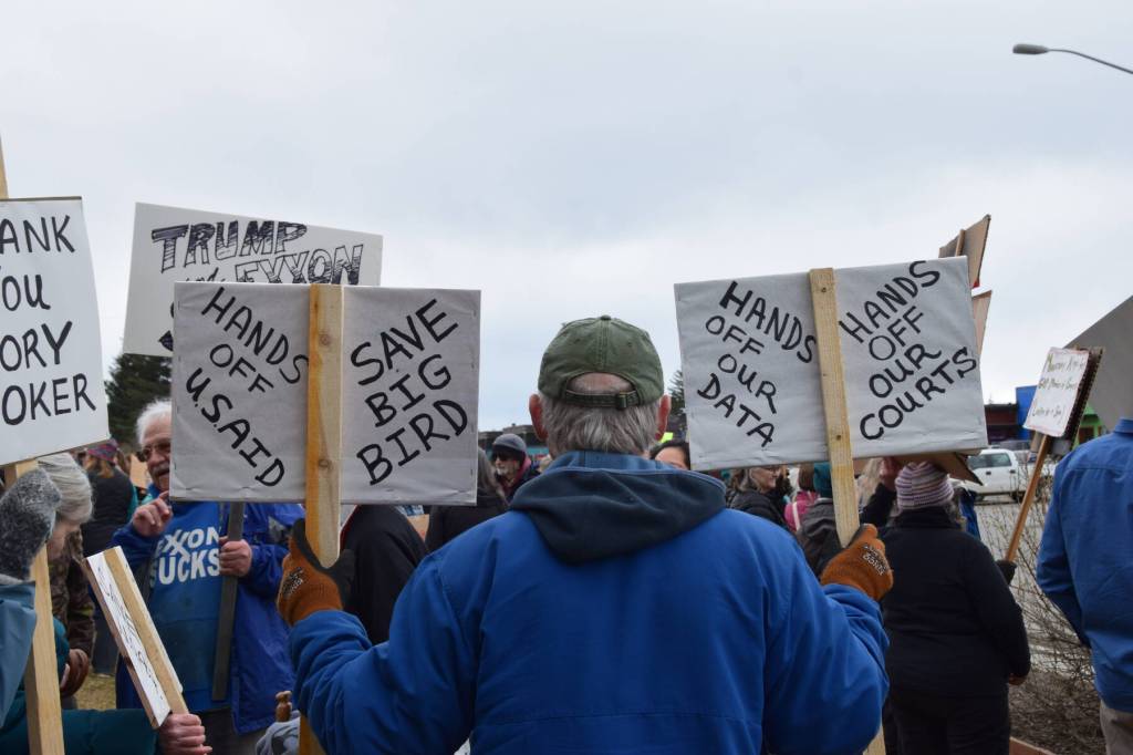 A protester in Homer holds up signs during the nationwide Hands Off! protest on Saturday, April 5 at WKFL Park in Homer, Alaska. (Chloe Pleznac/Homer News)