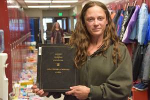 Lisa James holds up a book containing Nikolavesk History in the Nikolavesk School on Sunday, June 1, 2025, in Nikolavesk, Alaska. She said the book, along with trophies, photographs, and other school items will be boxed up and relocated to Homer Middle School upon Nikolavesk Schools closing on June 30. (Chloe Pleznac/Homer News)