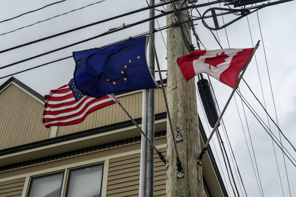 The U.S., Alaska state flag, and Canada flag wave in the wind in Skagway on Monday, June 16, 2025. (Jasz Garrett / Juneau Empire)