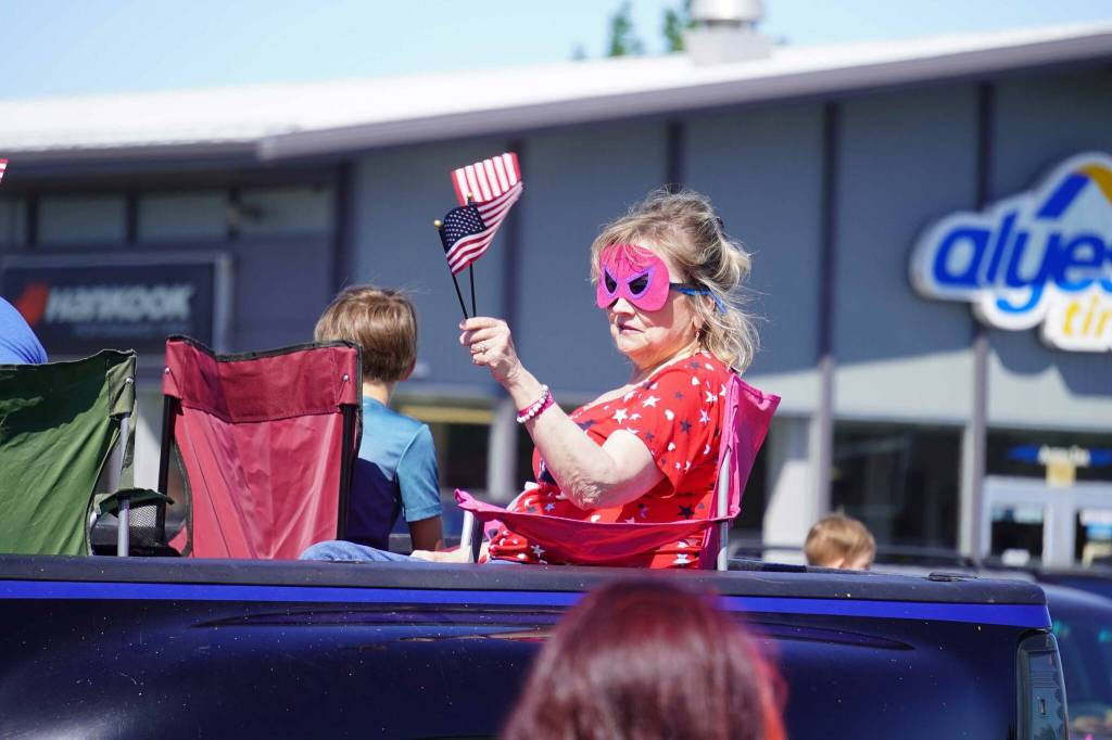 A masked woman waves a small American flag during a Fourth of July parade on South Willow Street in Kenai, Alaska, on July 4, 2025. (Photo courtesy Sarah Every)