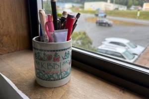 A vintage KBBI mug, repurposed and filled with various office supplies, rests in the Homer News office window on Friday, Aug. 8, 2025. (Chloe Pleznac/Homer News)