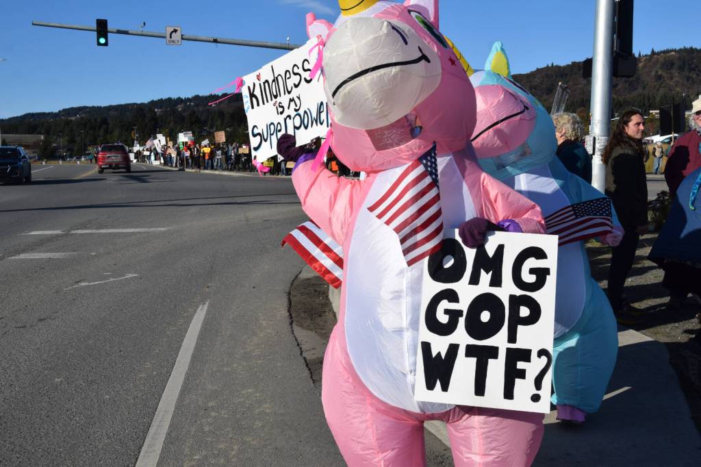 A protester in an inflatable unicorn costume holds up signs at the corner of Lake Street and Sterling Highway during the No Kings demonstration on Saturday, Oct. 18, 2025, in Homer, Alaska. (Delcenia Cosman/Homer News)