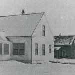 This is the only known photograph to show both the oldest modern building (white, in the foreground) and the oldest of the original buildings from the agricultural experiment station in Kenai (dark, directly behind the white building). Likely, this U.S. Fish & Wildlife Service image was taken in about 1949-50, shortly before the older building was destroyed. The smaller structure at far right remains unidentified.