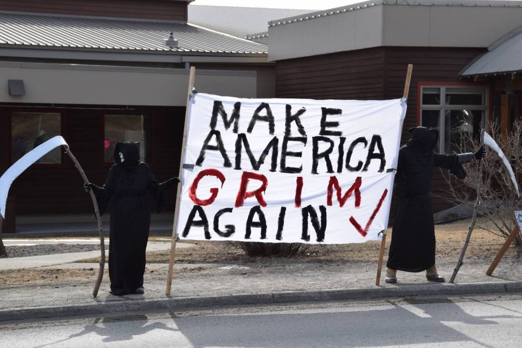 Two protesters dressed as grim reapers hold a large banner between them that reads Make America Grim Again with a large red check mark, during the No Kings protest on Saturday, March 28, 2026, in Homer, Alaska. One of the protesters, who did not give their name, said the banner was meant to represent how grim things currently are in the U.S. due to actions by the Trump administration. (Delcenia Cosman/Homer News)