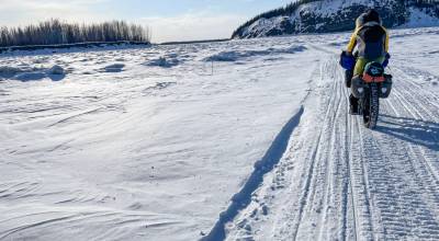 Forest Wagner rides his fat bike near Bishop Rock, right, a pinch point on the flow of the Yukon River, on April 5, 2026. (Photo by Ned Rozell)