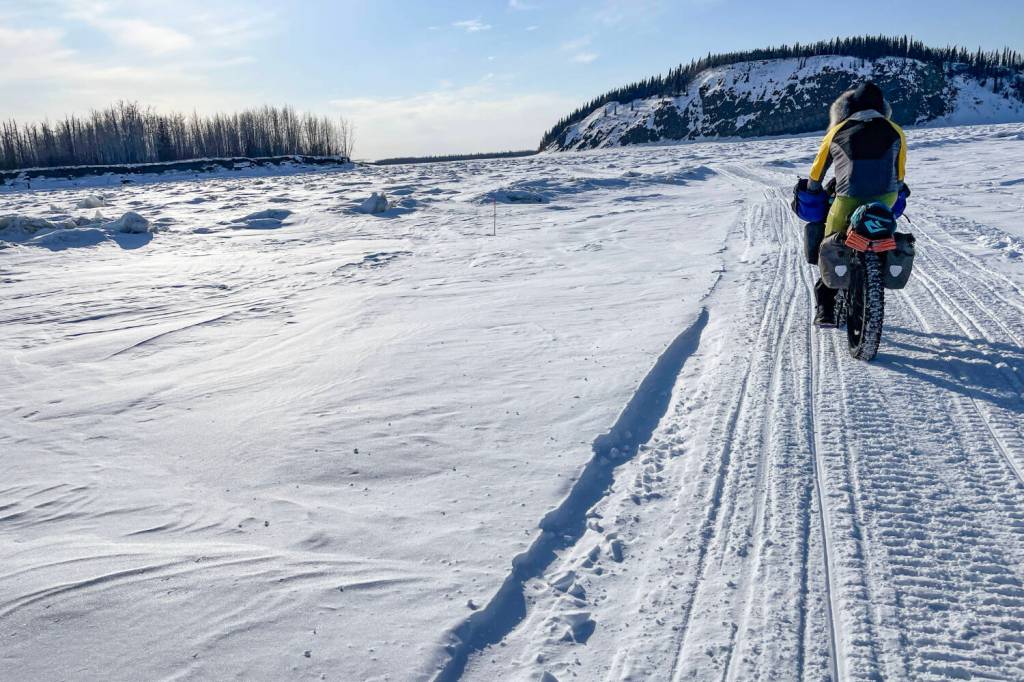 Forest Wagner rides his fat bike near Bishop Rock, right, a pinch point on the flow of the Yukon River, on April 5, 2026. (Photo by Ned Rozell)